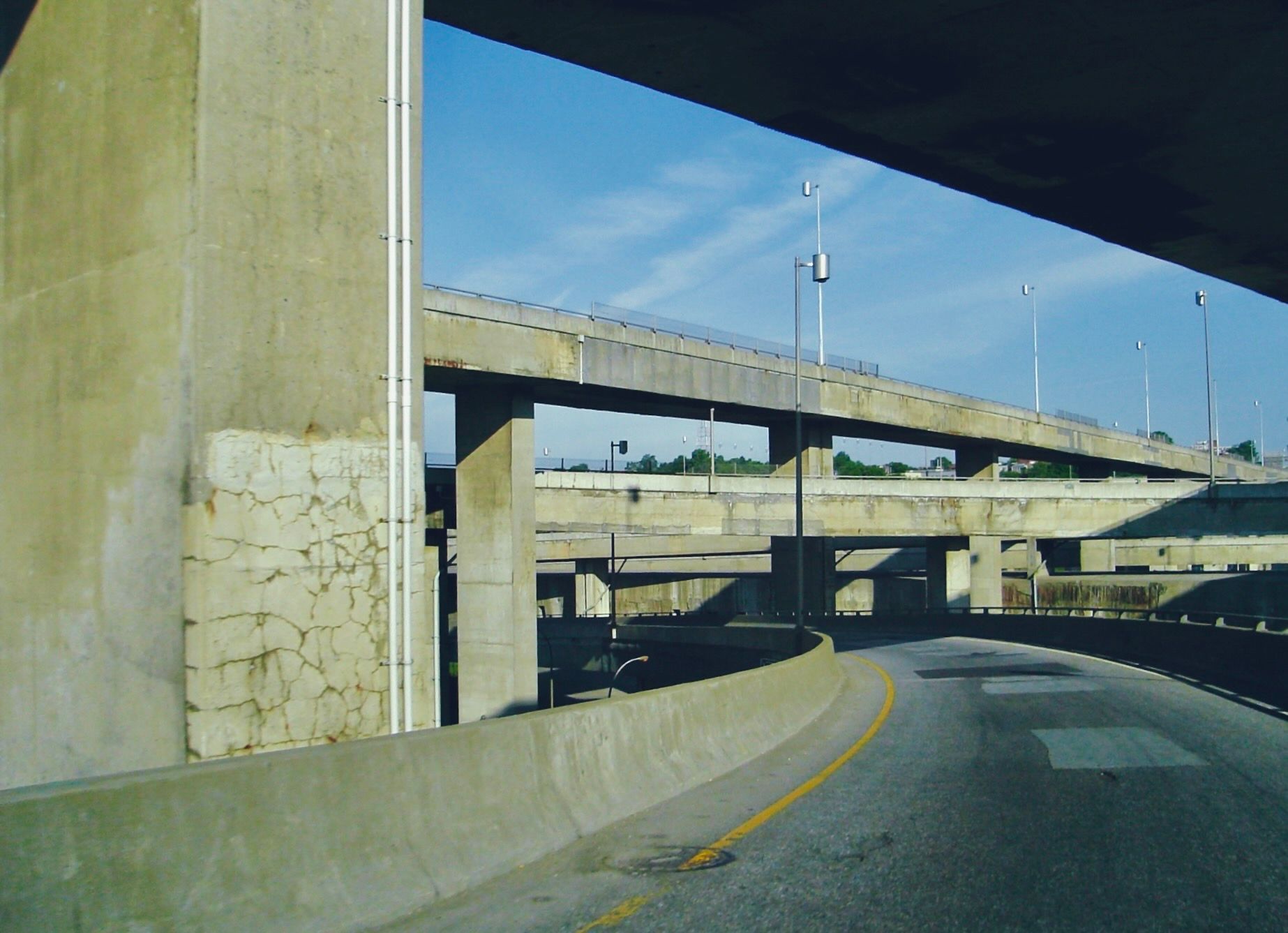 A cracked and discolored cement 4-level highway overpass under a blue sky.