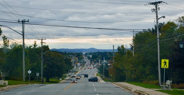 A photo of a street later in the day, looking down a long and mostly straight 4 lane stroad in a Maritime Canadian city.